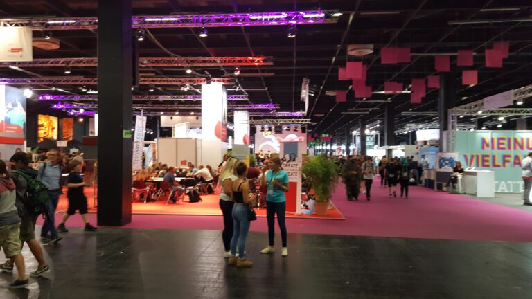 Blick in eine Gamescom-Messehalle 2019 mit Ständen, breiten Gängen und Besuchern.