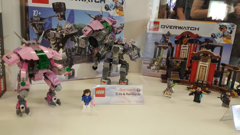 LEGO-Overwatch-Modelle und Verpackungen in einer beleuchteten Messevitrine.